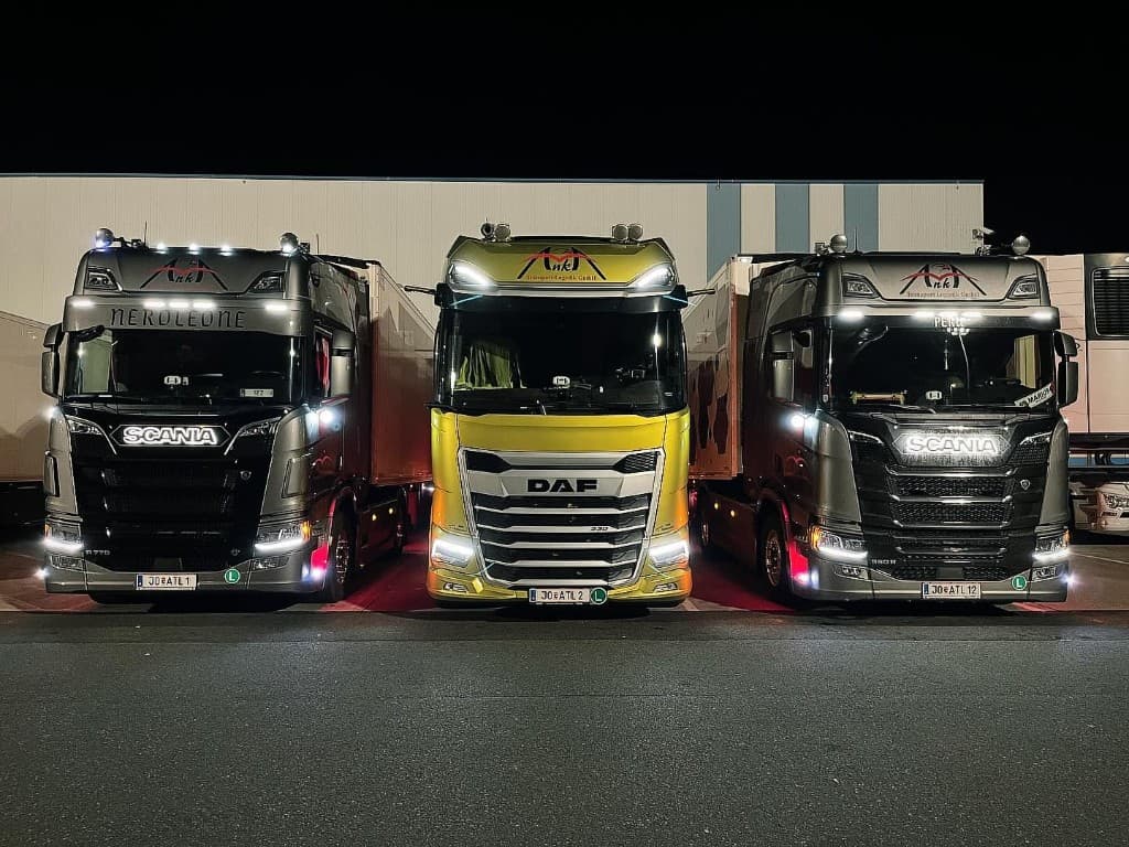Drei Lkw der Flotte vor dem Firmengebäude bei Nacht